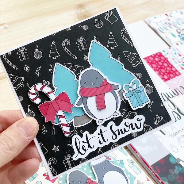 Close up of cute handmade penguins card with penguin and scarf, candy cane and christmas trees