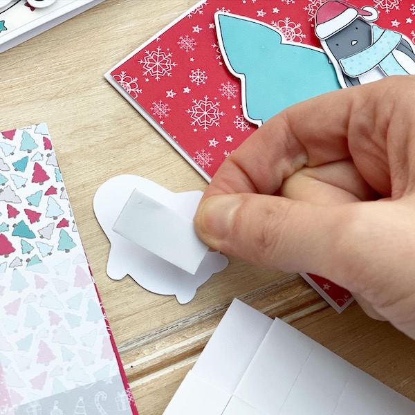 Hand sticking a foam adhesive pad on the back of a paper penguin