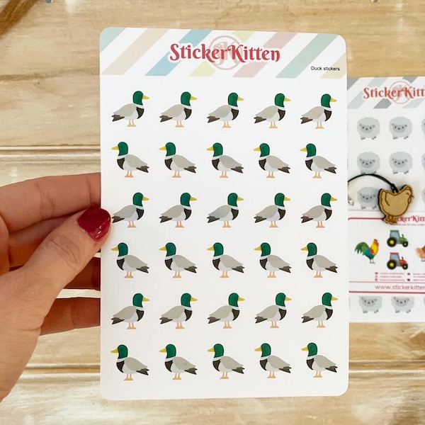 A sheet of cute duck stickers by StickerKitten held up over a wooden board with other farmyard stickers in the background
